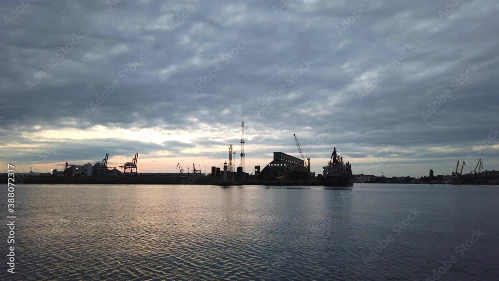 View after sunset of port facilities and industrial cranes behind calm water surface. Light wind at blue hour. Gray cloudscapes. View after sunset of port facilities and industrial cranes behind calm water surface. Light wind at blue hour. Gray cloudscapes.