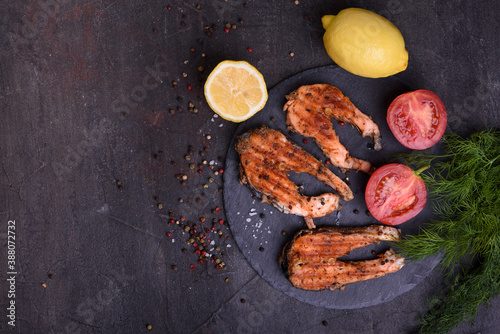 Grilled fresh salmon steak with pepper and lemons on dark table. Top view. Fish for healthy food.
