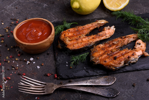 Grilled fresh salmon steak with pepper and lemons on dark table. Fish for healthy food