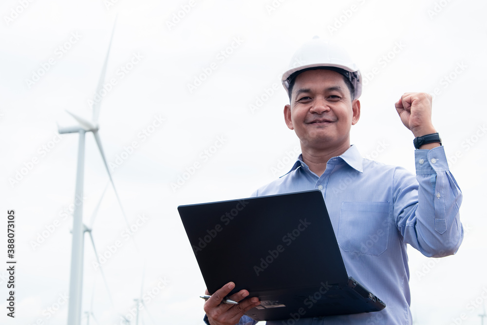 Engineers windmills wearing face mask and working on laptop with the wind turbine in background Engineers windmills wearing face mask and working on laptop with the wind turbine in background