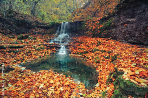 Waterfall in the autumn forest. Silky smooth stream. The stones are covered fallen yellow leaves.