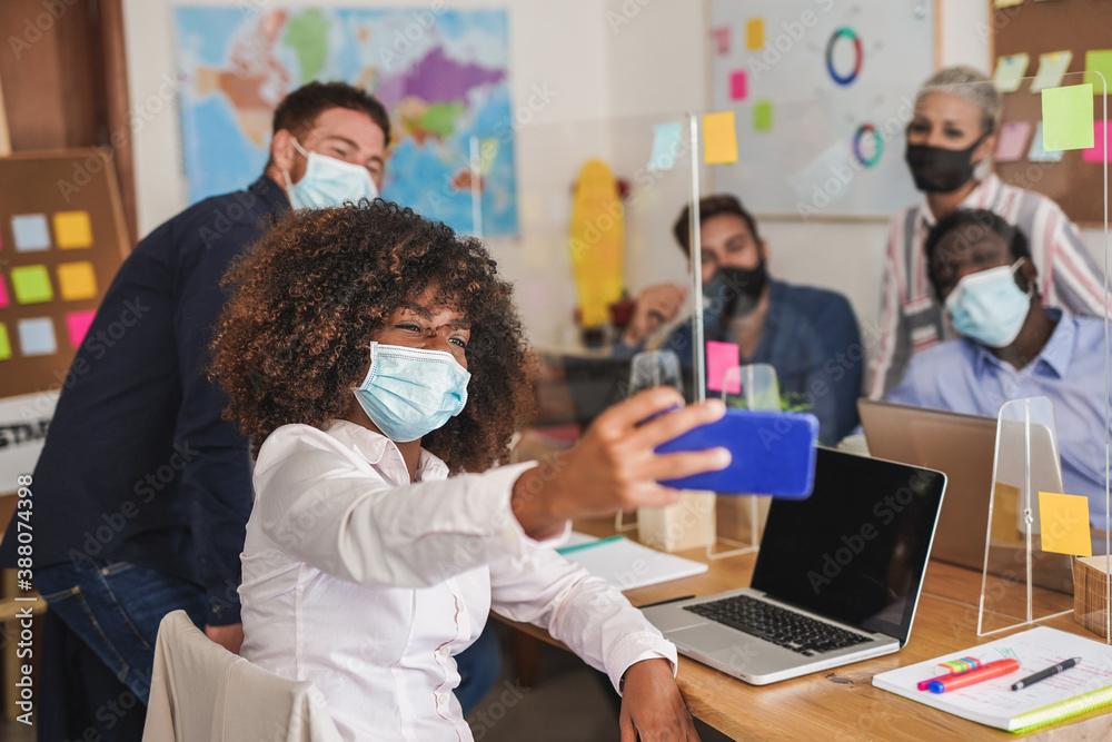 Happy multiracial staff taking a selfie with smartphone in the office - Coworking people wearing surgical face mask for coronavirus Happy multiracial staff taking a selfie with smartphone in the office - Coworking people wearing surgical face mask for coronavirus
