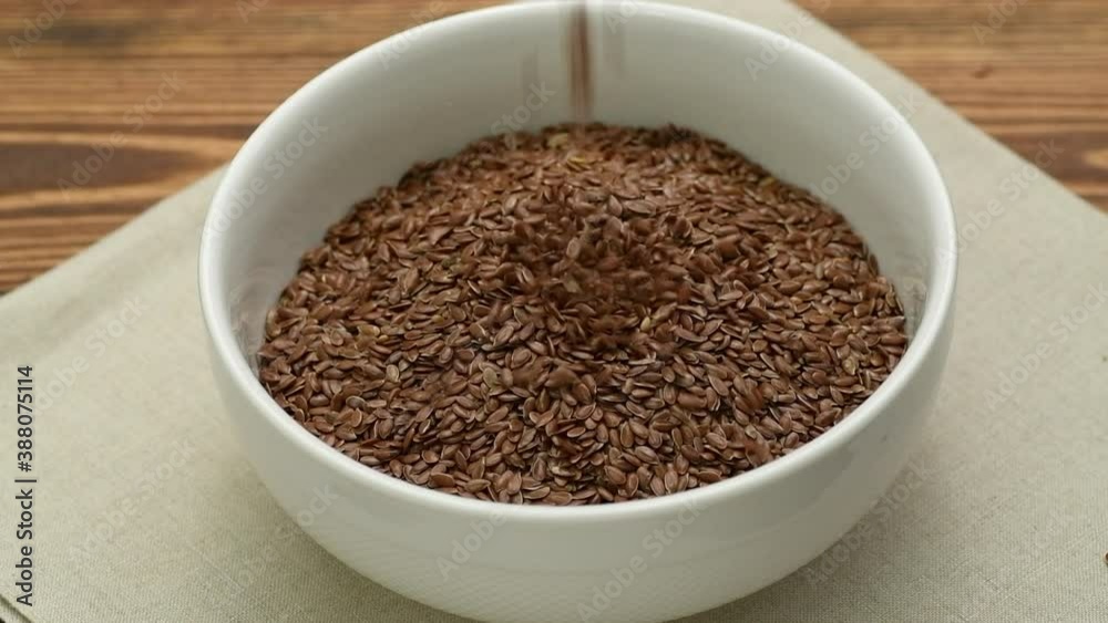 Flax seeds falling into a white bowl, slow motion Flax seeds falling into a white bowl, slow motion