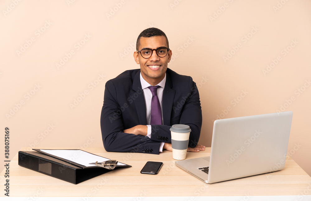 Young business man in his office with a laptop and other documents keeping the arms crossed in frontal position Young business man in his office with a laptop and other documents keeping the arms crossed in frontal position