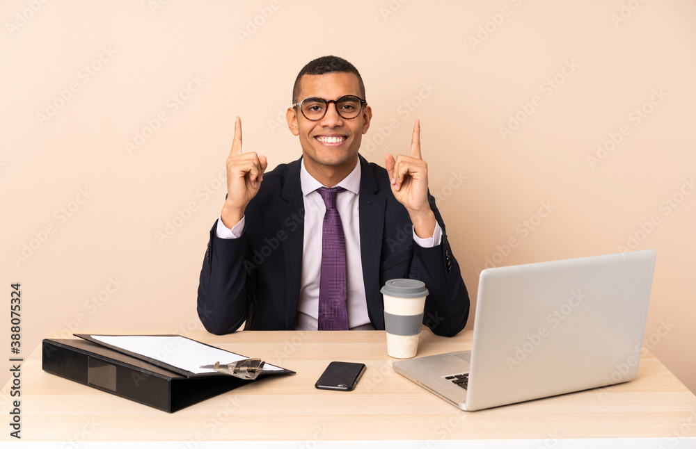 Young business man in his office with a laptop and other documents pointing up a great idea Young business man in his office with a laptop and other documents pointing up a great idea