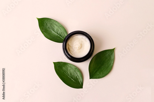 Round cosmetic cream container on the beige background,fresh juicy green leafs around.Organic cosmetics concept.Flat lay style,copy space.