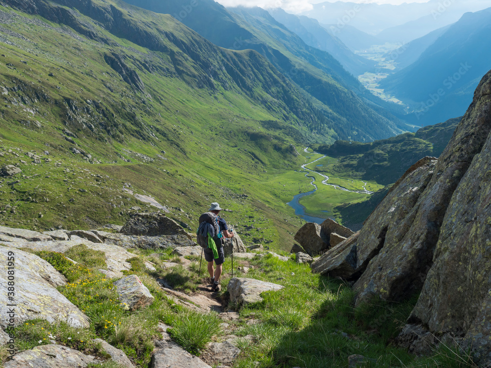 Lonely man hiker with heavy backpack at Stubai hiking trail, Stubai Hohenweg at green summer alpine mountain valley with winding river spring stream. Tyrol, Austrian Alps Lonely man hiker with heavy backpack at Stubai hiking trail, Stubai Hohenweg at green summer alpine mountain valley with winding river spring stream. Tyrol, Austrian Alps