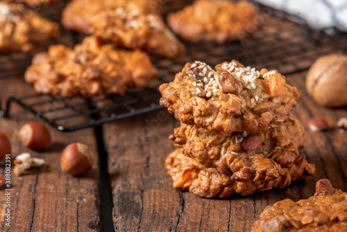 Homemade oatmeal cookies with various nuts and sesame seeds on an old dark wooden table. Tasty and healthy dessert, vegetarian and vegan food. Rustic style. Oatmeal cookies close-up.
