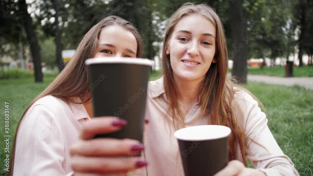 Caucasian young stylish cheerful girls having picnic at nature while sitting on grass and drinking beverages. Celebration cheers concept Caucasian young stylish cheerful girls having picnic at nature while sitting on grass and drinking beverages. Celebration cheers concept