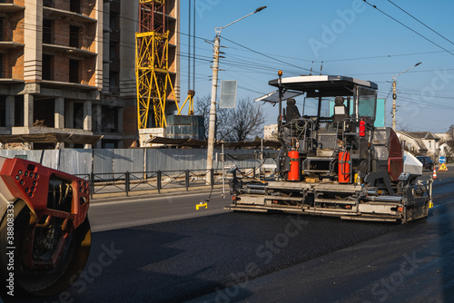 Industrial asphalt paver machine laying fresh asphalt and a Heavy road roller with vibration roller compactor press new hot asphalt on a road construction site.