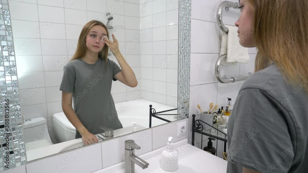 Attractive young woman hold cotton pad cleansing clean face skin with cleaning lotion. Happy attractive girl removing make up looking in mirror enjoying healthy beauty treatment. Skincare concept. Attractive young woman hold cotton pad cleansing clean face skin with cleaning lotion. Happy attractive girl removing make up looking in mirror enjoying healthy beauty treatment. Skincare concept.