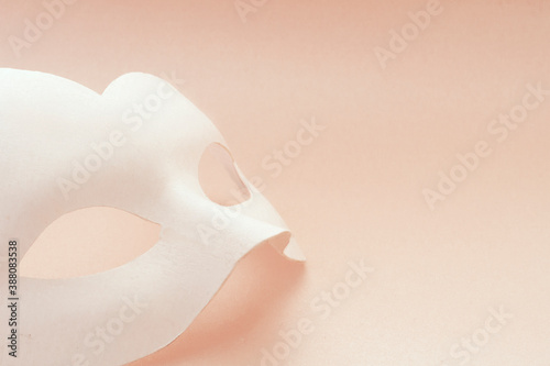 White carnival mask on a pink background. The mask lies vertically.