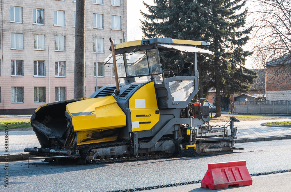 Industrial asphalt paver machine laying fresh asphalt on road construction site on the street. A Paver finisher placing a layer of a new hot asphalt on the roadway on a construction site. Repairing.