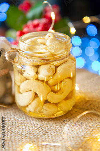 Jar with honey and nuts on a light bokeh background Honey with cashews in glass small jars on a brown cloth. Organic and healthy foods.