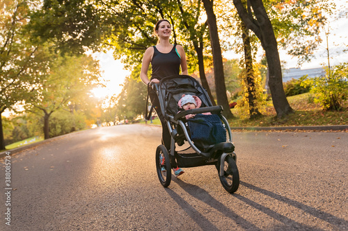 Beautiful young mother with her daughter in jogging stroller running outside in autumn nature photo