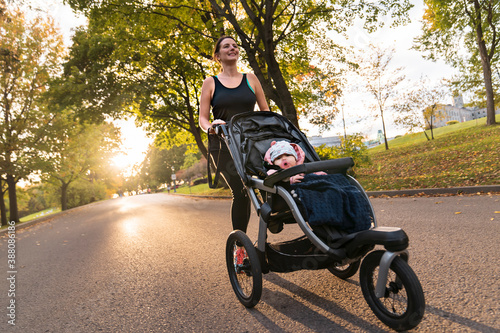 Beautiful young mother with her daughter in jogging stroller running outside in autumn nature