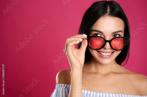 Beautiful woman wearing sunglasses on pink background, closeup. Space for text