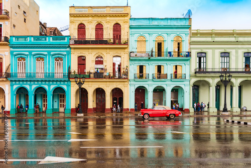 red classic car in front of colorful houses in old havana on a rainy day © Michael Barkmann