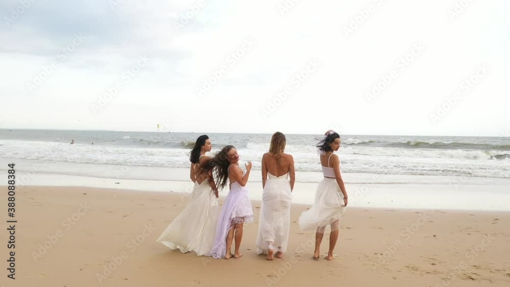 4 beautiful girls in white wedding dresses stand with their backs to the camera on the seashore. slow motion video of four brides from the back against the sea 4 beautiful girls in white wedding dresses stand with their backs to the camera on the seashore. slow motion video of four brides from the back against the sea