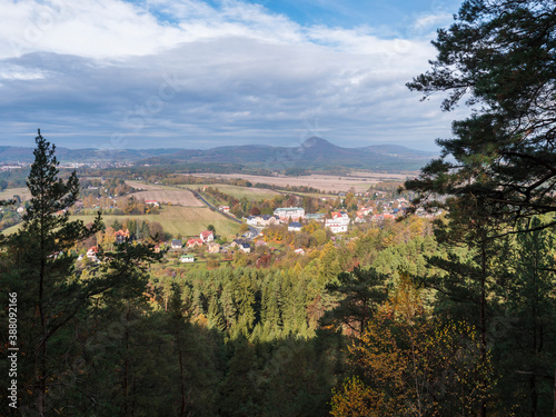 View from Hrabencina vyhlidka lookout on village Sloup v cechach in luzicke hory, Lusatian Mountains with autumn colored deciduous and coniferous tree forest and green hills, blue sky, white clouds photo
