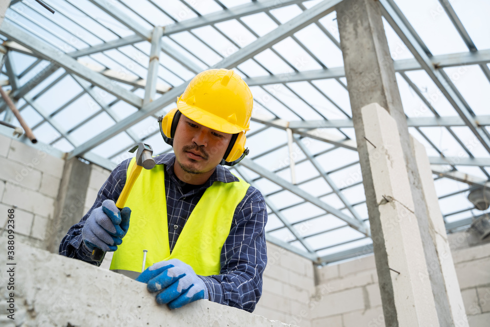 industrial worker building exterior walls in the house under construction,Using hammer for laying bricks in cement. industrial worker building exterior walls in the house under construction,Using hammer for laying bricks in cement.