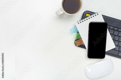 a phone with a screen mockup, a coffee cup of writing supplies,with a computer mouse a pens, a notepad on a white wooden table background. Top view of the work area, copy space