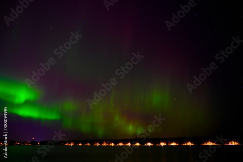 Aurora borealis green beam of northern lights with purple tail beside a lake under starry sky