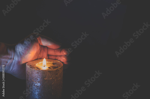 one burning candle with hand protecting the flame copy space