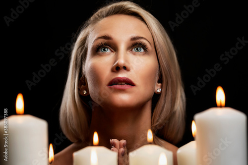 Young woman prays with candles. Beautiful blonde on a black background. Close-up.