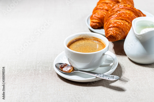 Croissants and cup of coffee in the morning light, sunlight shadow, on a linen fabric. Morning breakfast concept.