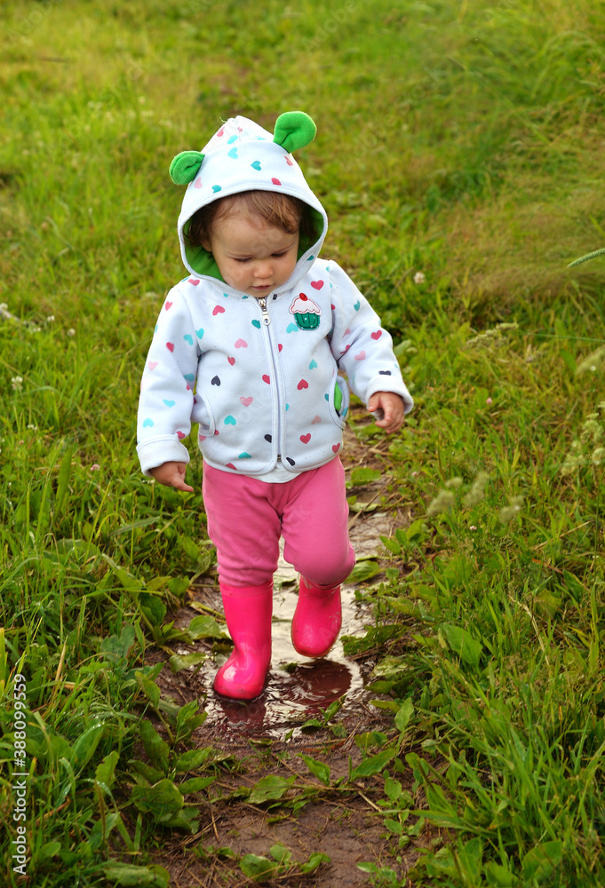 Little girl in red boots walks along path with rain puddles Little girl in red boots walks along path with rain puddles