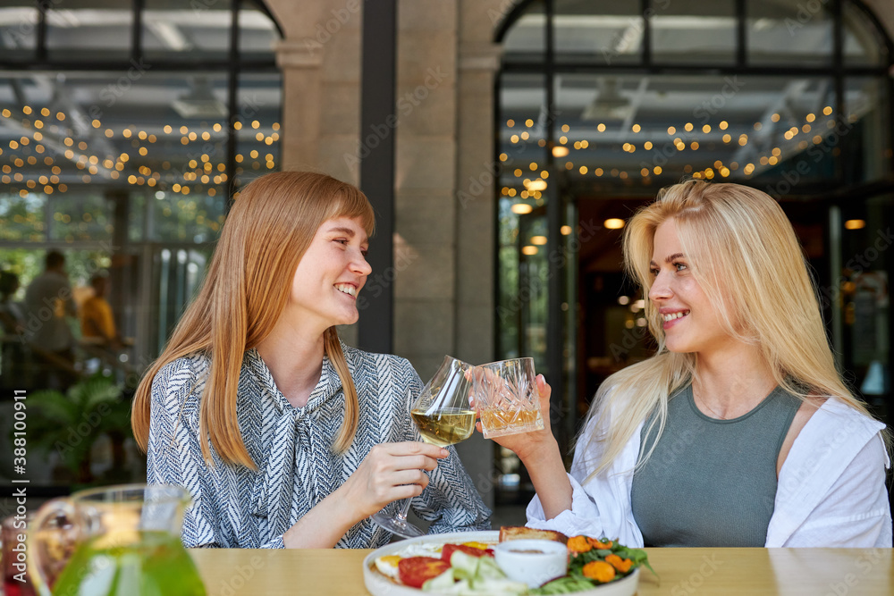 two positive caucasian women enjoy spending time together in restaurant, blonde females have talk and drink beverages, enjoy meal. they haven't seen each other for a long time