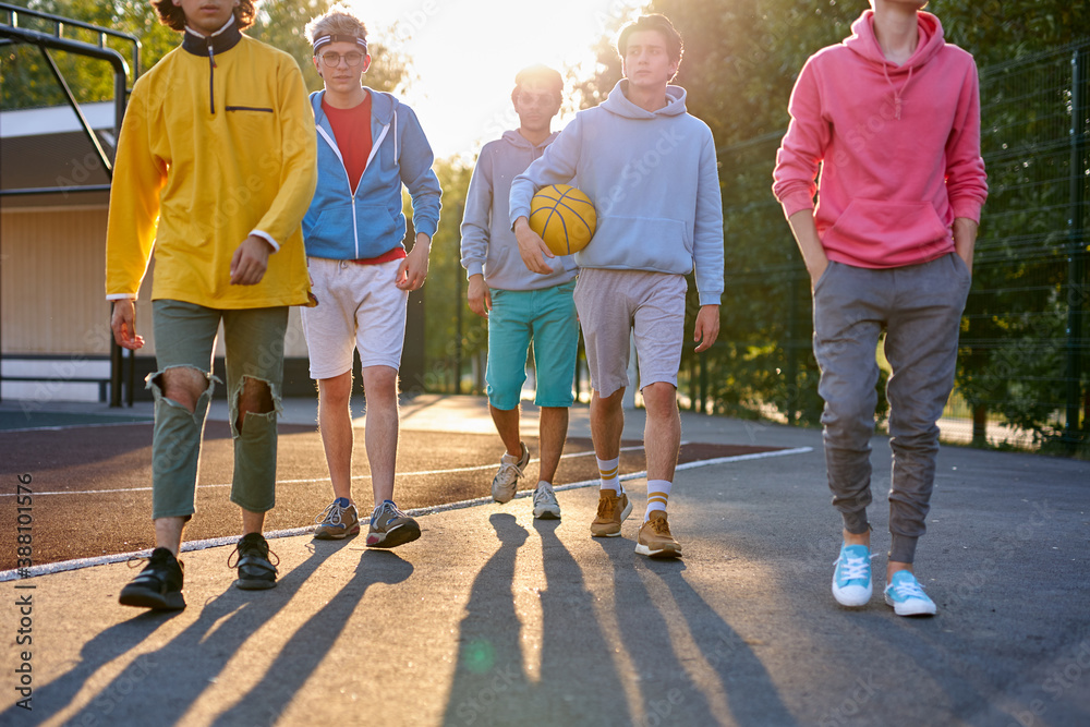 Naklejka premium sportive young boys going to play basketball in the street, handsome teenagers have friendly talk while they are going at playground