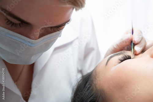 Close-up of a beautiful asian woman on eyelash extension procedure. Double volume false eyelashes. Lashmaker at work.
