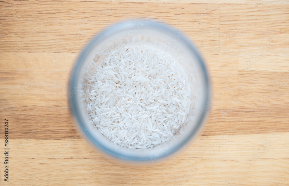 White long-grain basmati rice, jasmine in a glass jar on a wooden oak tabletop background top view. Ideas for storing bulk food, cereals at home in the kitchen.