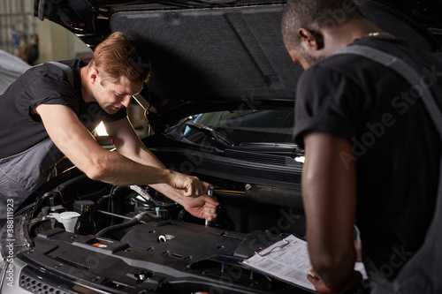multi-ethnic team of african and caucasian men working in auto service together, friendly men in uniform repair the car hood