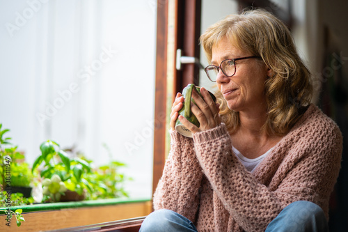 Adult woman taking tea pensive looking out the window photo