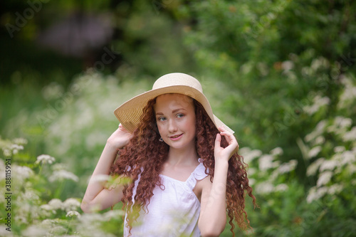 Cute red girl in straw hat on a flowering clearing at a picnic with fruit