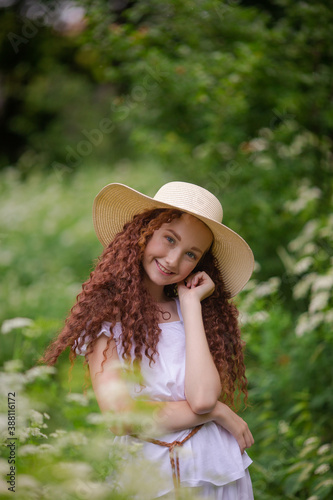 Cute red girl in straw hat on a flowering clearing at a picnic with fruit