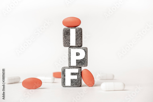 a group of white and red pills and cubes with the word IPF Idiopathic pulmonary fibrosis on them, white background. Concept carehealth, treatment, therapy. photo