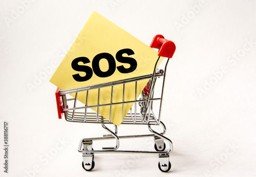 Shopping cart and text SOS on yellow paper note list. Shopping list, business concept on white background.