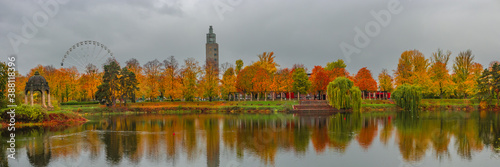 Panorama over city park and lake in Autumn colors at rainy day with heavy sky, Ferris wheel and observation tower, Magdeburg, Germany.