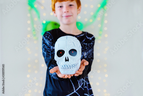 Horizontal view of little kid with skeleton spider costume holding a trick or treat Halloween basket shaped as a skull. Halloween costume party for family and children. Seasonal and festive concept.