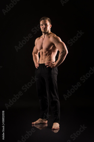 Strong athletic man showes naked muscular body on a dark background. © lik13vvs