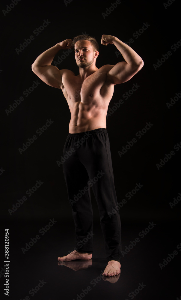 Strong athletic man showes naked muscular body on a dark background.