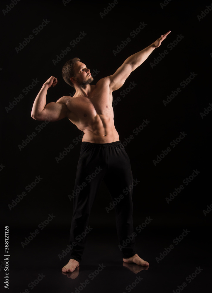 Strong athletic man showes naked muscular body on a dark background.