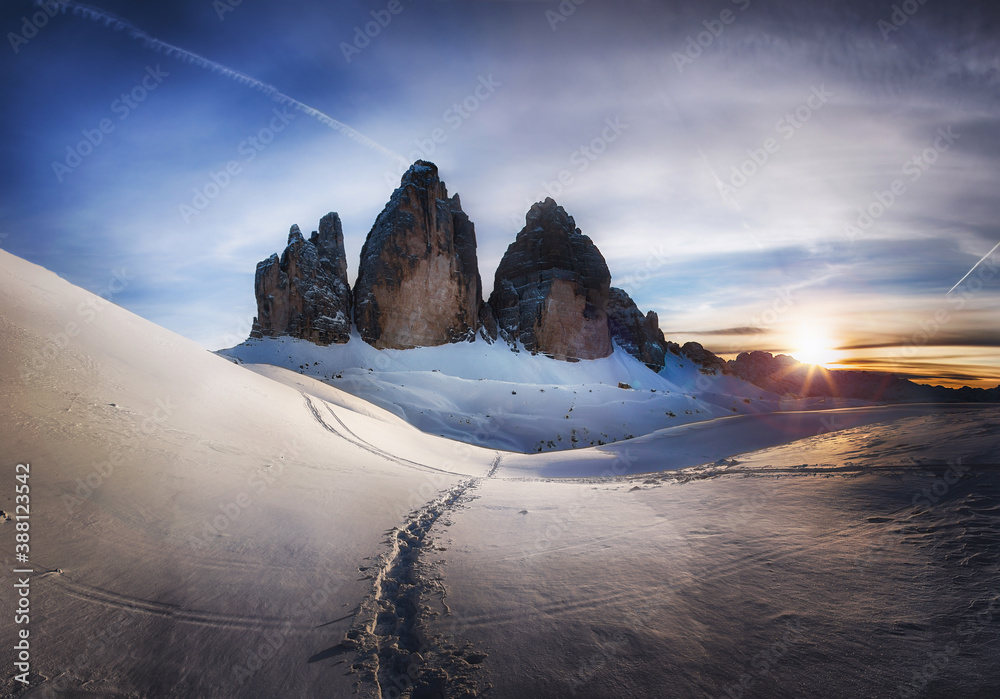 Winter mountain landscape in the Dolomites Alps. Mountains at sunset against a background of snowy trail. Traces of ski tourists in the snow. Tre Cime di Lavaredo, Italy. Classic postcard view.