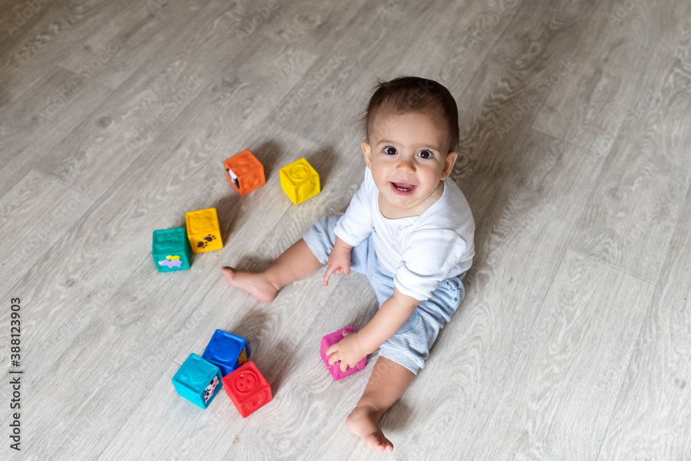 Naklejka premium Baby is playing with blocks. A little boy in white bodysuit at home. Beautiful portrait of a toddler. Big-eyed baby. Remote education. Distance learninig 