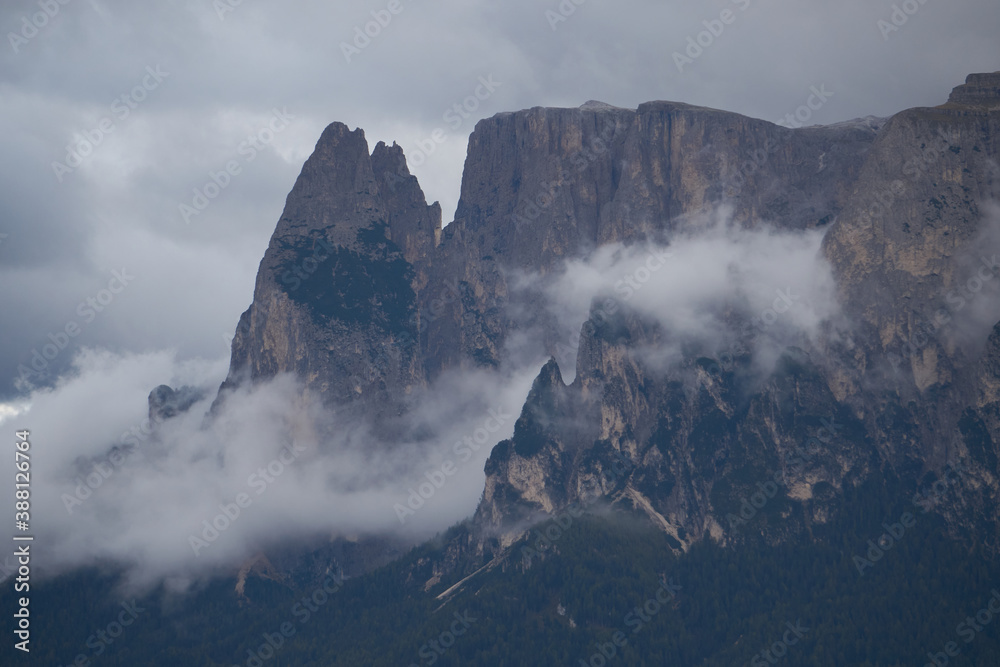 Dramatic dolomite rock between clouds with green forest below
