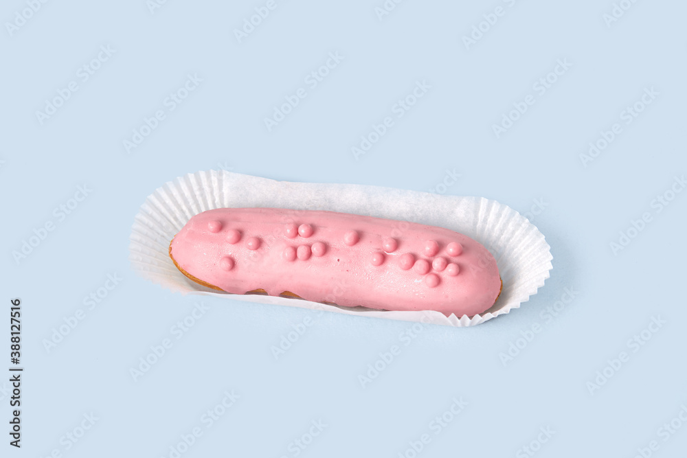 Bright Eclair in pink glaze in wrapping paper, sprinkled with colorful pink jelly beans, balls. Isolated on a blue background. Bright Eclair in pink glaze in wrapping paper, sprinkled with colorful pink jelly beans, balls. Isolated on a blue background.